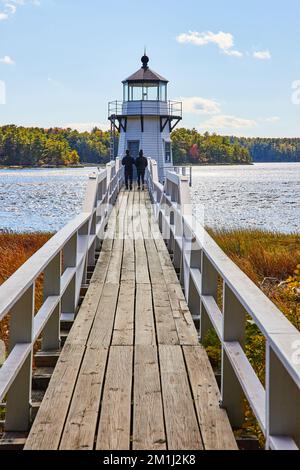 Le pont en bois mène au petit phare blanc du Maine avec deux touristes marchant Banque D'Images