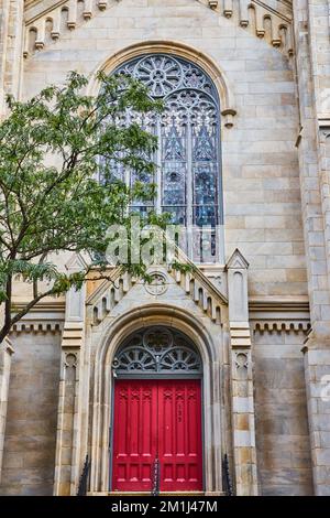 Devant de l'église chrétienne avec des portes rouges vibrantes et des vitraux Banque D'Images