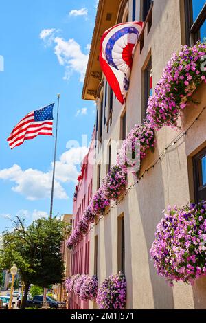 Drapeau américain et couleurs par mur recouvert de fleurs de boîte de fenêtre rose Banque D'Images