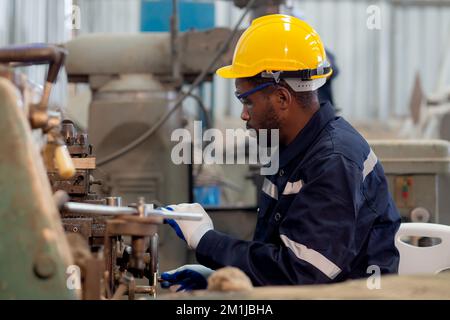 Jeune ingénieur noir homme utilisant la machine de tour pour préparer la production à l'usine industrielle, technicien ou de la main-d'œuvre de machines de maintenance à l'atelier plac Banque D'Images