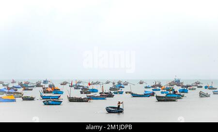 Un pêcheur vietnamien solitaire guide son coracle en se laquant son filet de pêche par une flottille de bateaux de pêche traditionnels amarrés sur la plage My Khe, Danang, V Banque D'Images