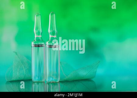 ampoules cosmétiques. Produits de beauté.ampoules transparentes et feuilles vertes squelettes sur un fond turquoise vert flou. Banque D'Images