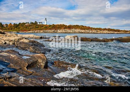 Côte du Maine avec des vagues qui s'écrasant sur des rochers peu profonds et un phare en arrière-plan Banque D'Images