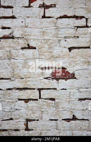 Mur de briques rouges peint en blanc avec de la peinture fissurée et une brique rouge exposée Banque D'Images