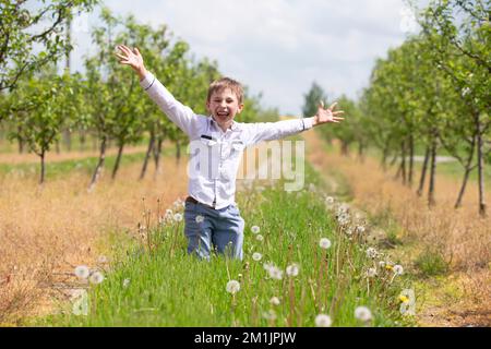 Joyeux garçon se réjouit dans le jardin de printemps. Les vacances scolaires d'été ont commencé. Banque D'Images