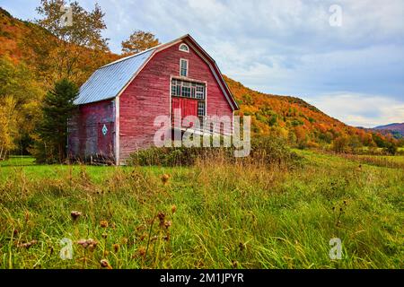 Grange rouge dans les champs de campagne entouré de montagnes de feuillage d'automne Banque D'Images