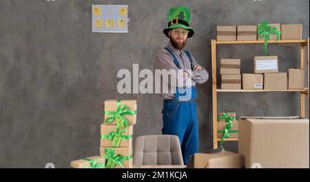 Un vendeur heureux portant un chapeau Leprechaun dépêchez-vous pour livrer des cadeaux le jour de Patrick debout dans l'entrepôt de l'atelier avec des cadeaux, livraison rapide express, Banque D'Images