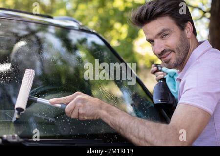 homme mature nettoyant le pare-brise de voiture avec un chiffon et un spray Banque D'Images