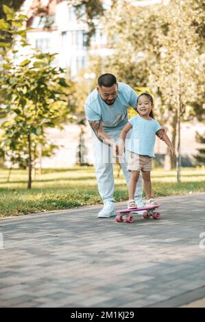 Papa enseignant à sa fille de monter à bord d'un skate board Banque D'Images