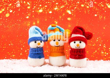 Bonhomme de neige tricoté en chapeaux et chandails rouges, bleus et orange sur fond rouge avec des lumières de Noël dorées. Joyeux Noël et nouvel an 2023 Banque D'Images