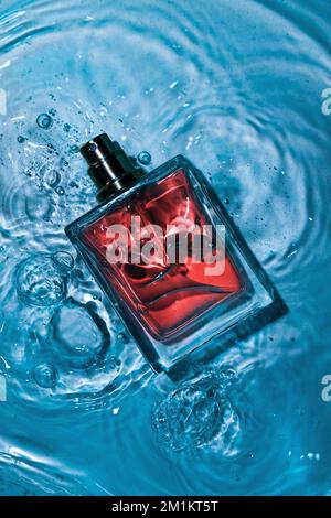 Vue de dessous d'une bouteille de parfum vaporisée sur une table en verre de couleur bleue. Banque D'Images