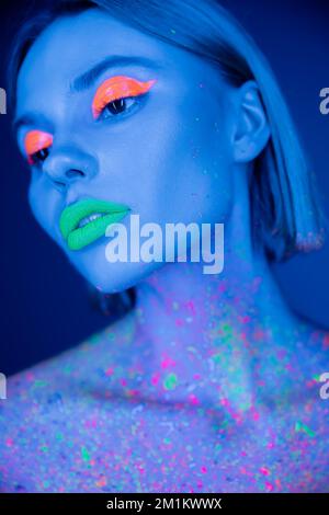 portrait de jeune femme avec maquillage fluorescent et peinture néon sur le corps isolé sur bleu foncé, image de stock Banque D'Images
