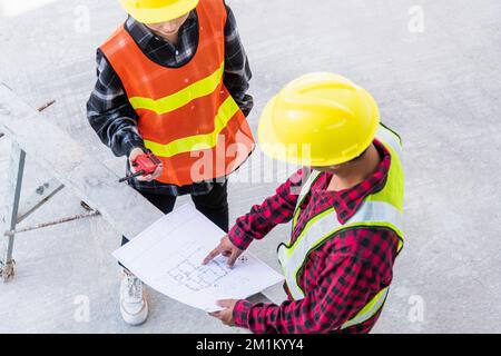 L'architecte et le client discutent de l'aide à la création d'un plan avec le plan du bâtiment au plancher du chantier de construction Banque D'Images