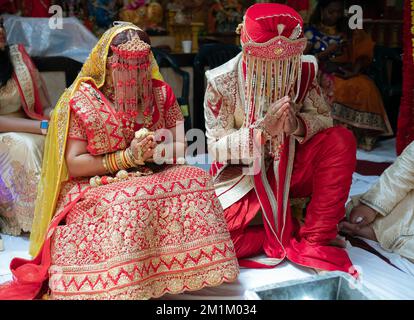 Lors d'un mariage hindou, la mariée et le marié sont assis avec leurs mains jointes et portant des coiffures de sehra. À Queens, New York. Banque D'Images