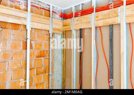 Vue sur les profils en bois et en métal pour les cloisons et le faisceau de câbles rouges ondulés longs et isolés qui pendent, le bâtiment est en dessous de la const Banque D'Images