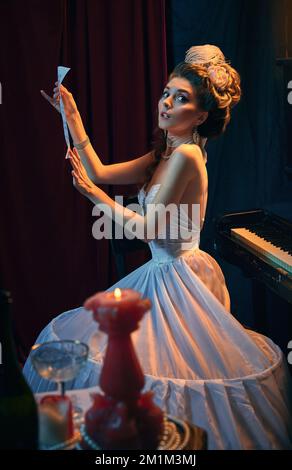 Portrait de la belle jeune femme à l'image de la personne médiévale, musicien en robe blanche tendre assis au piano avec une nouvelle composition musicale. Comparaison Banque D'Images