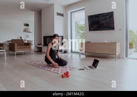 Jeune belle femme exercice, étirement et pratiquer le yoga avec formateur via vidéoconférence dans lumineux Sunny Loft Appartement. En bonne santé Banque D'Images