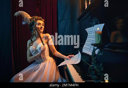 Inspiration. Portrait de la belle jeune femme à l'image de la personne médiévale, princesse assise au piano en robe blanche tendre et jouant Banque D'Images