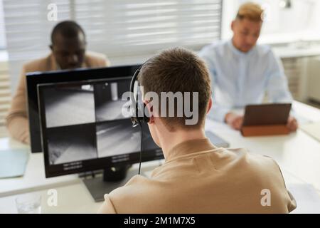 Vue arrière d'un homme portant un casque regardant des vidéos de surveillance sur un moniteur du centre de sécurité Banque D'Images