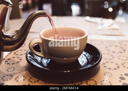 Tisane rouge chaude au restaurant. visite le thé chaud de la bouilloire à la tasse assis à table avec le thé versant de la nappe Banque D'Images