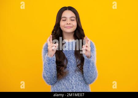 Un adolescent tenant les doigts croisés pour Bonne chance. La jeune fille prie et espère que les rêves deviennent vrais, isolé sur fond jaune. Banque D'Images