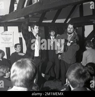 1970, historique, musique folklorique, homme avec une guitare acouiste debout jouant dans une salle à poutres apparentes dans un pub, Angleterre, Royaume-Uni. Une affiche sur un mur annonce : « an Evening of Folk », avec Shirley & Dolly Collins, Dave & Toni Arthur. Bob & Carol Pegg et Dave & Dave au Stevenage College of approfondissement Education. Les bras Defffe ?? Banque D'Images