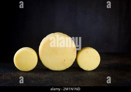 Beaucoup de différentes sortes de têtes de fromage sur table sombre. Têtes de fromage dures moyennes sur planche à découper en bois. Concept de saine alimentation biologique. Fromage fait à la main Banque D'Images