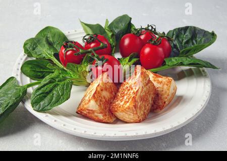 Fromage caillé mozzarella halloumi frit avec tomates cerises et épinards verts sur une table en béton gris Banque D'Images