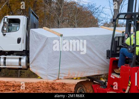 Homme utilisant un chariot élévateur travaillant au déchargement de pièces de construction de matériaux de construction Banque D'Images