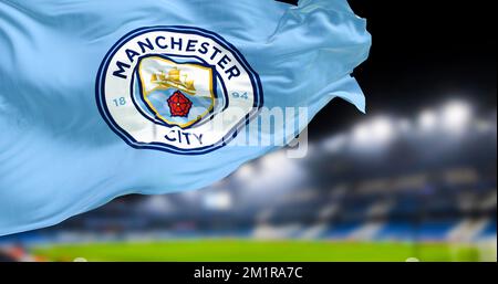 Manchester, Royaume-Uni, novembre 2022 : le drapeau du Manchester City football Club agité dans le stade du club brouillé en arrière-plan la nuit. Illustration réaliste 3D. Banque D'Images