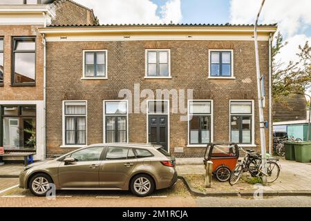 une voiture garée devant une maison avec deux vélos dans la rue à côté et un vélo appuyé contre le mur Banque D'Images