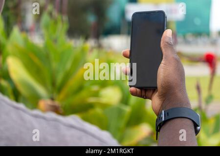 Main d'un fermier africain tenant un smartphone noir. Banque D'Images