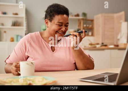 Portrait d'une femme âgée noire riant avec joie tout en écoutant un message vocal via un smartphone Banque D'Images