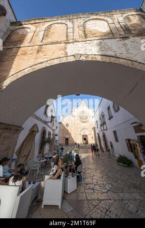 Cathédrale Santa Maria Assunta de la place Largo Arcid Teodoro Trinchera et café illuminés en soirée, encadrés par l'Arco Scoppa à Ostuni Banque D'Images