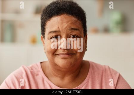Portrait chaleureux et ton grand-mère noir souriant à l'appareil photo dans un cadre de cuisine confortable Banque D'Images