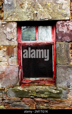 Une fenêtre en bois peint en rouge avec des intempéries dans un mur de chalet en ardoise avec des intempéries. Banque D'Images