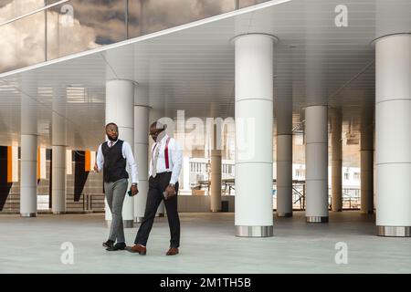 Portrait de deux hommes d'affaires à la peau sombre marchant et parlant devant un bâtiment moderne extérieur. Réunion à l'extérieur Banque D'Images