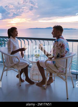 Un couple d'hommes et de femmes qui boivent des cocktails sur le balcon d'un hôtel à Pattaya Thaïlande au coucher du soleil. Banque D'Images