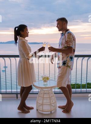 Un couple d'hommes caucasiens et de femmes thaïlandaises boivent des cocktails sur le balcon d'un hôtel à Pattaya Thaïlande au coucher du soleil. Banque D'Images