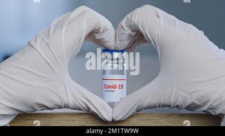 Gros plan de la main femelle dans des gants médicaux en latex blanc faisant la forme du coeur montrent le signe de l'amour espoir confiance approbation près d'une bouteille de dose de vaccin de Banque D'Images