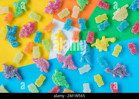 Une couche plate de bonbons colorés en forme de dinosaure et d'ours recouverts de poudre aigre sur fond coloré Banque D'Images