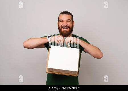 Souriant barbu homme portant le vert tient quelques sacs de shopping qu'il a acheté pour des cadeaux. Banque D'Images