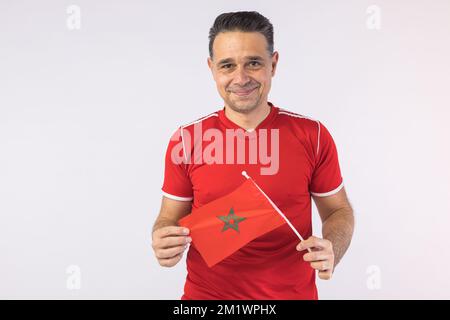 Homme portant une chemise marocaine rouge, portant un drapeau marocain. Sport, coupe du monde et concept de fan. Banque D'Images