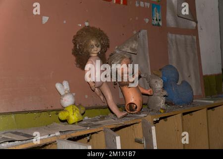 Vieilles poupées abandonnées et jouets animaux sur un mobilier en bois à l'intérieur d'un jardin de Kinder de tchernobyl Banque D'Images