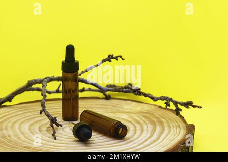 Maquette de flacons en verre brun avec couvercle compte-gouttes sur panneau en bois. Vider les flacons en verre avec pipette, branche d'arbre sur fond jaune. Concept de médecine Banque D'Images