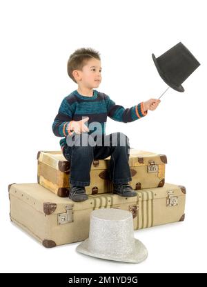 Garçon isolé en Jean et pull-over rayé assis sur quelques vieilles valises joue avec une baguette et un chapeau de dessus. Banque D'Images