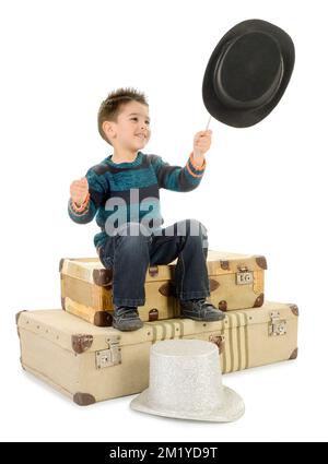 Garçon isolé en Jean et pull-over rayé assis sur quelques vieilles valises joue avec une baguette et un chapeau de dessus tout en le regardant. Banque D'Images