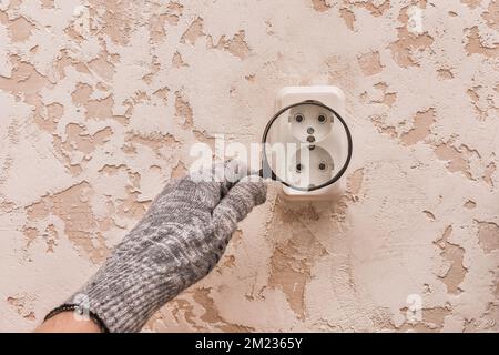 La main d'un ouvrier de construction masculin en gants de protection examine à travers une loupe la connexion des appareils. Banque D'Images