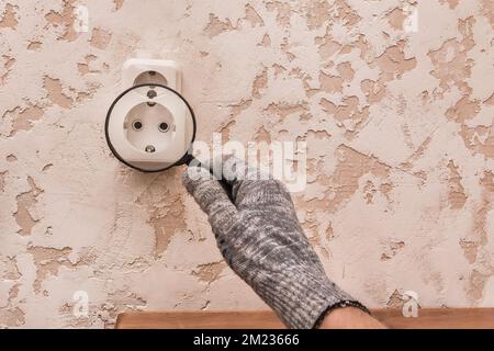 La main d'un travailleur masculin en gants de protection examine à travers une loupe la connexion des appareils dans la maison. Banque D'Images