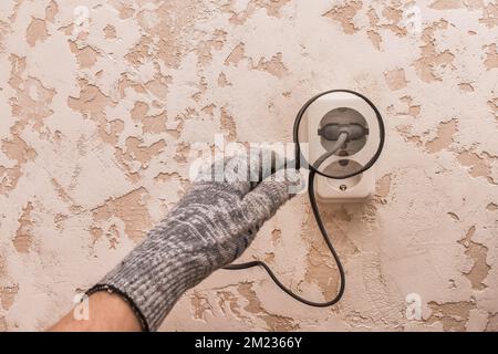 La main d'un ouvrier de construction masculin en gants de protection examine à travers une loupe la connexion des appareils dans la maison. Banque D'Images